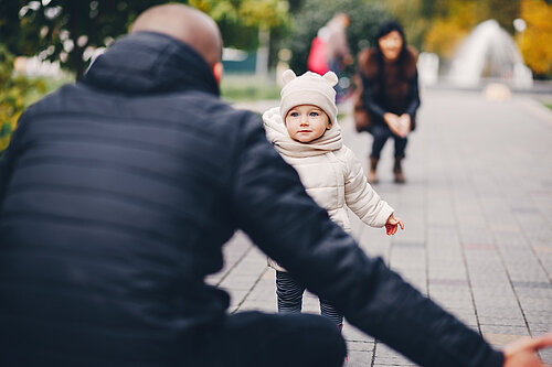 Man facing away from the camera with arms open as child runs towards him