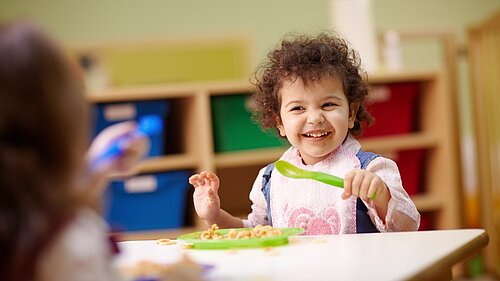 A toddler eating food off a plate with a spoon.